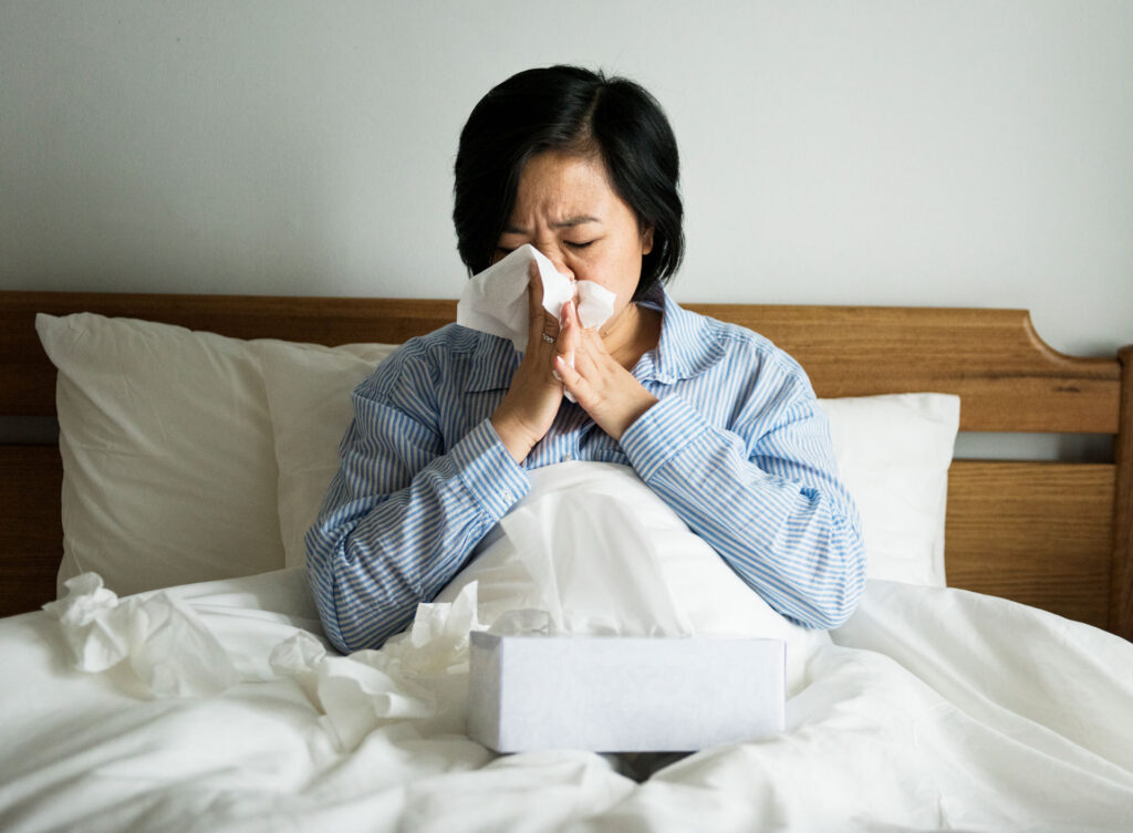 woman in bed sneezing into tissue