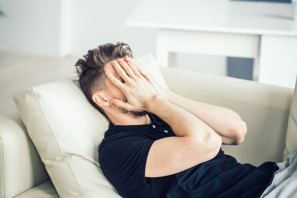 stressed male with hands over face lying on a couch
