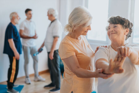 senior physical trainer helping senior woman stretch