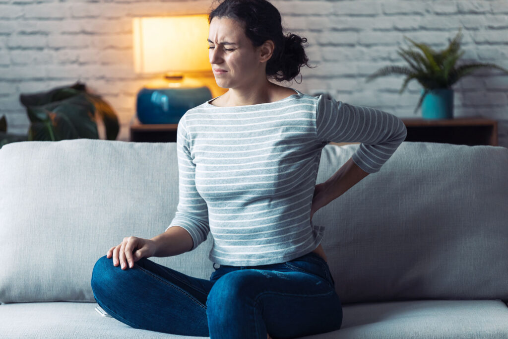 young woman sitting on couch experiencing back pain
