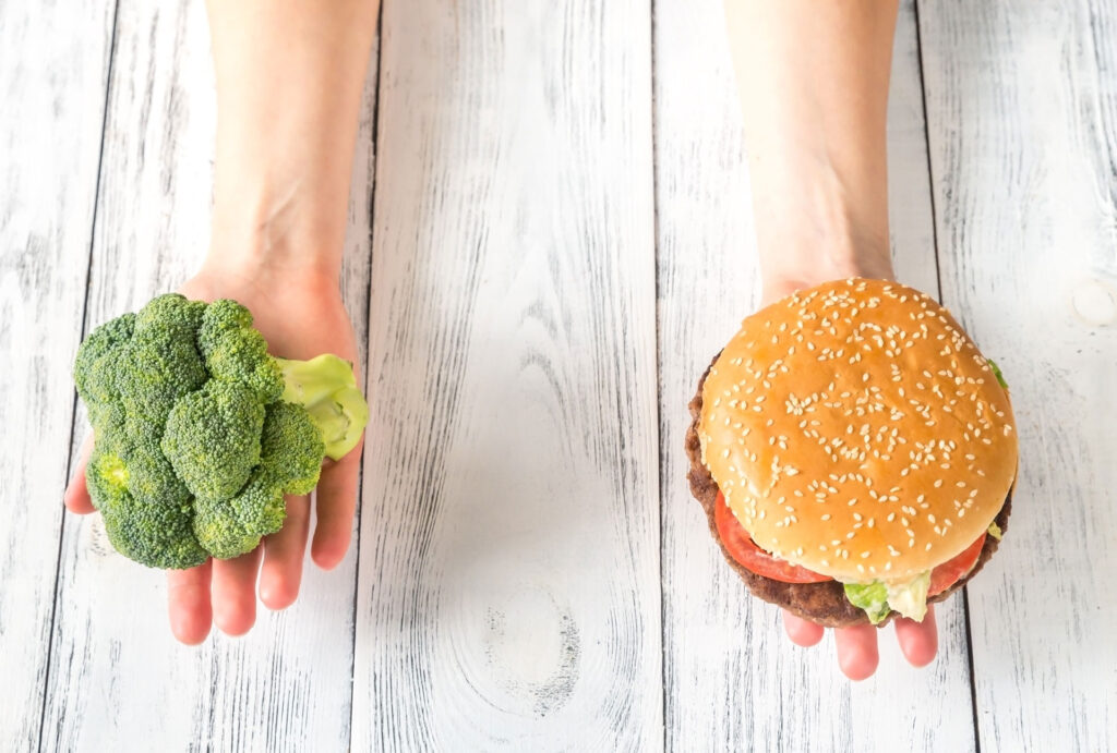 broccoli being held up next to a hamburger demonstrating healthy vs unhealthy food