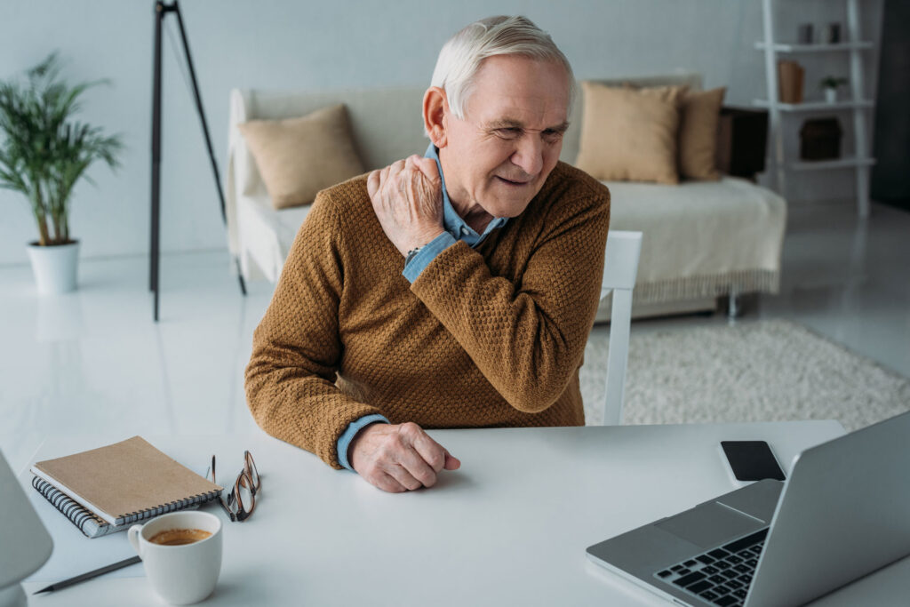 senior man experiencing back pain while working on laptop computer