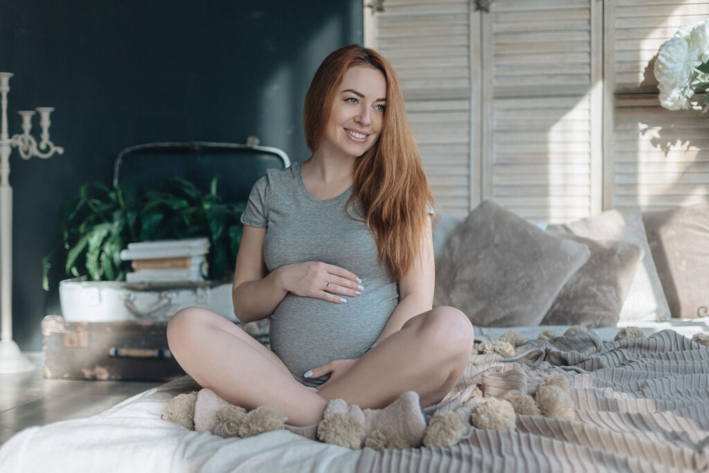 pregnant woman happily sitting on bed