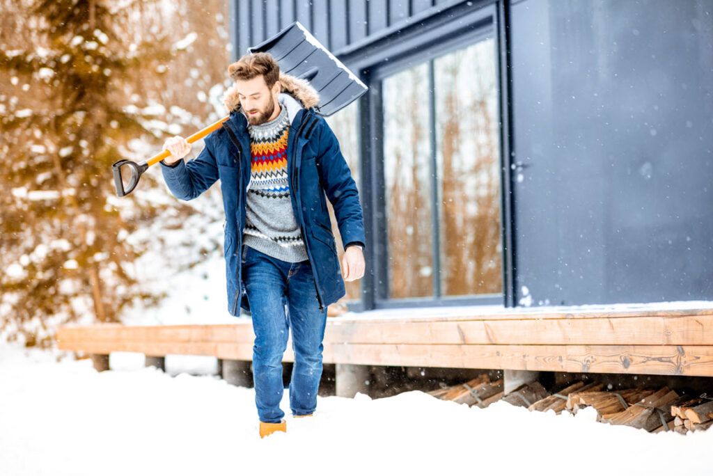 man holding snow shovel outside of house