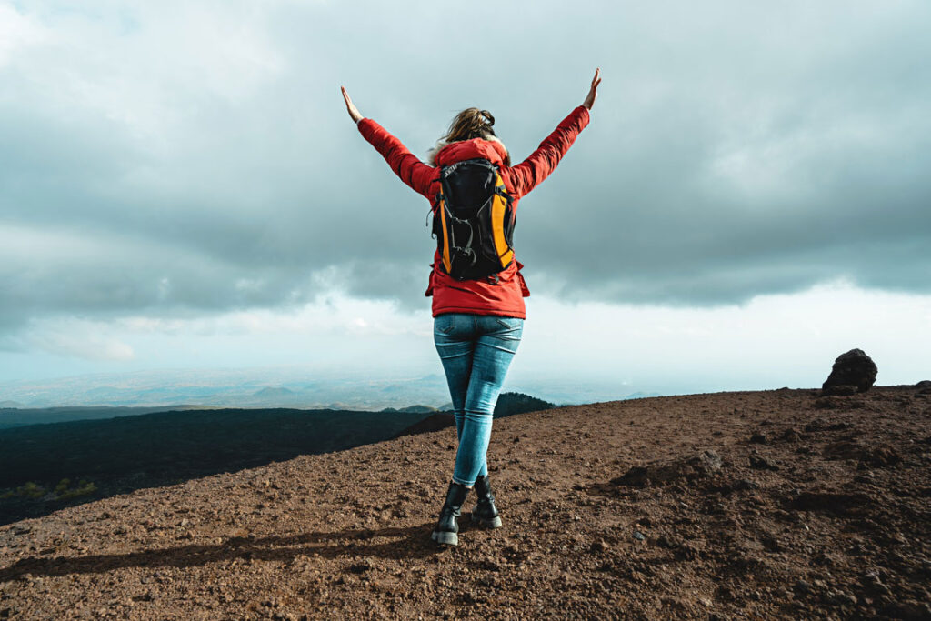 back view of female hiker on top of a mountain holding her hands up in accomplishment