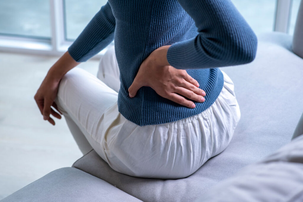 female sitting on couch holding her lower back in pain