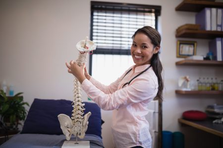 portrait-of-smiling-female-therapist-examining-art-2023-11-27-04-54-12-utc Doctor holding model of spine