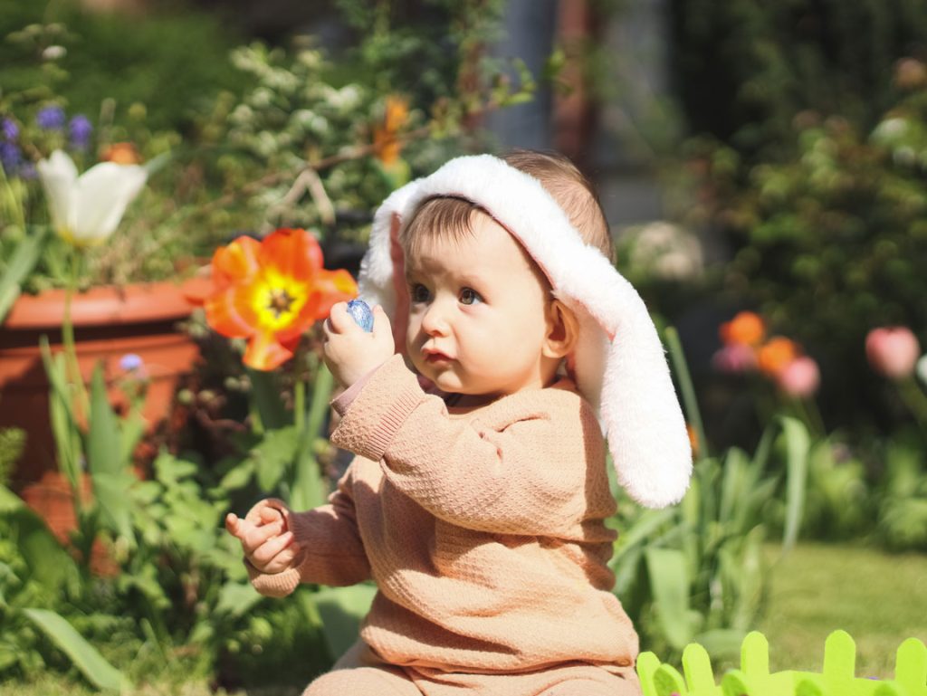 beautiful-caucasian-baby-girl-with-a-headband baby in spring yard wearing bunny ears