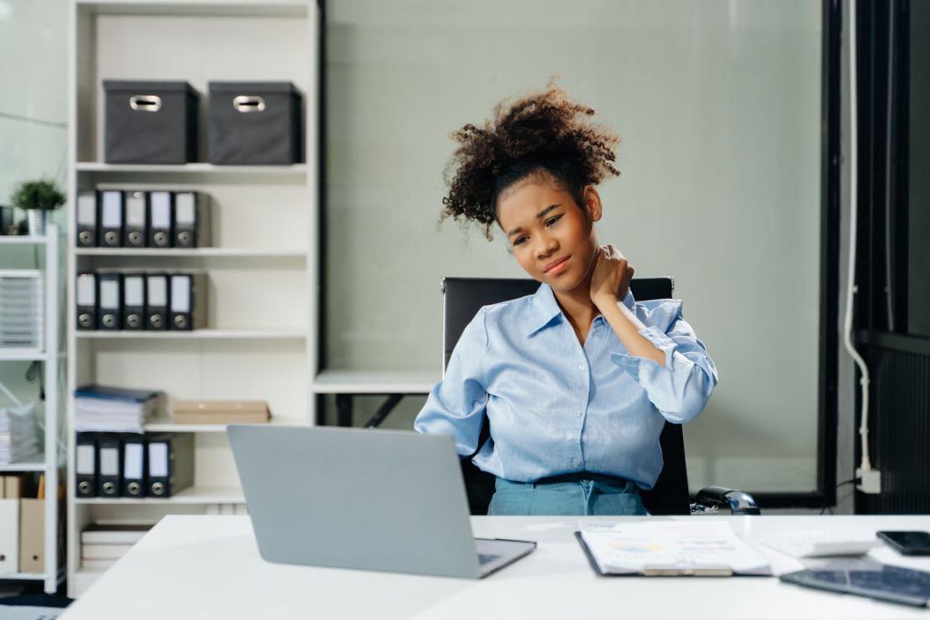 overworked-young-businesswoman-office-worker female worker at desk holding her neck in pain